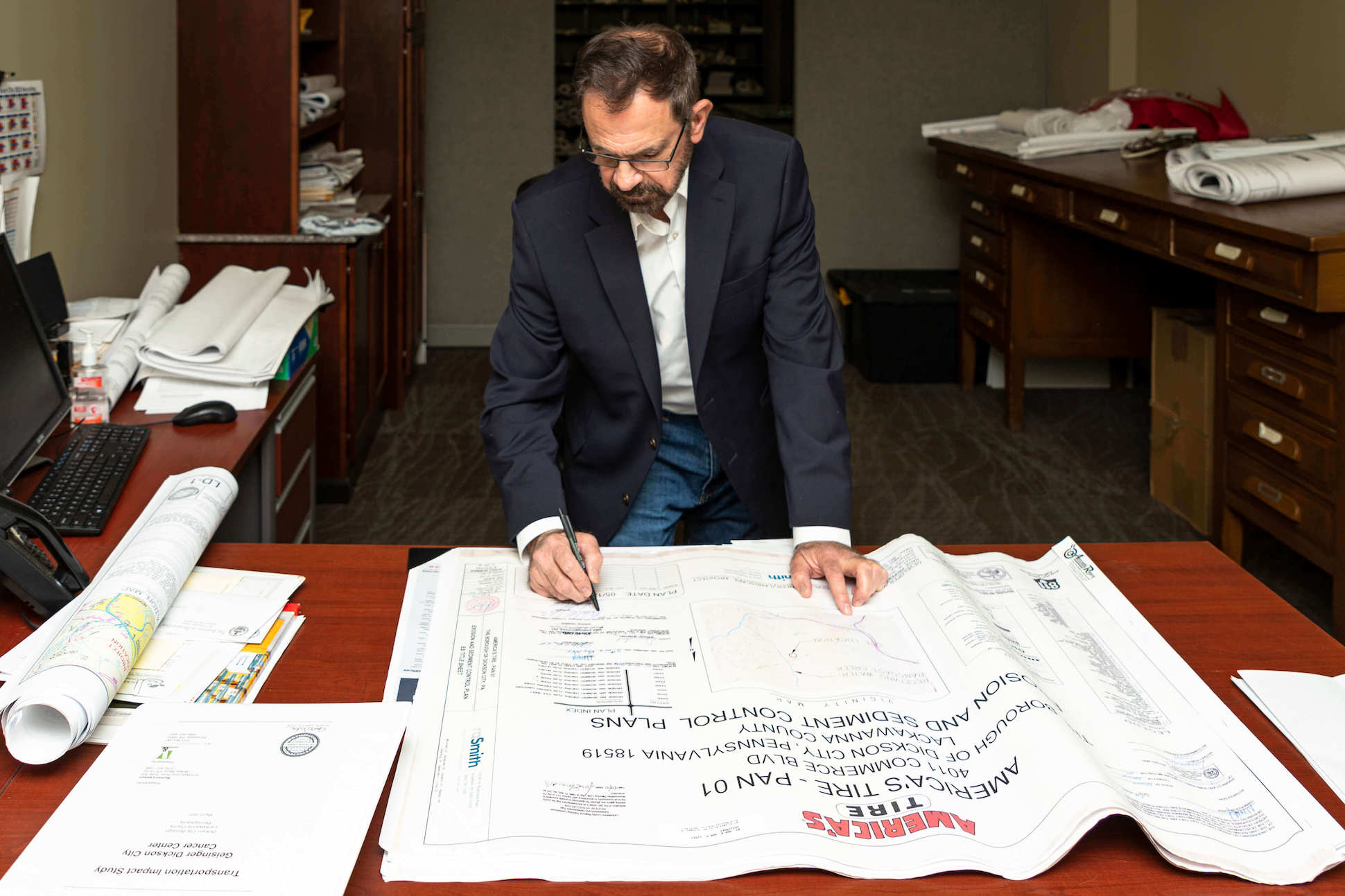 Mike Fedorka standing over plans the size of a desk and signing them.